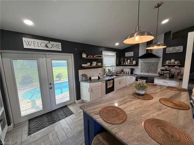 Kitchen with white cabinets, backsplash, hanging light fixtures, a kitchen bar, and recessed lighting