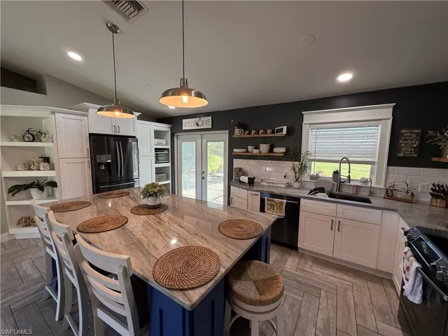 Kitchen featuring open shelves, white cabinetry, black appliances, decorative light fixtures, and light stone countertops