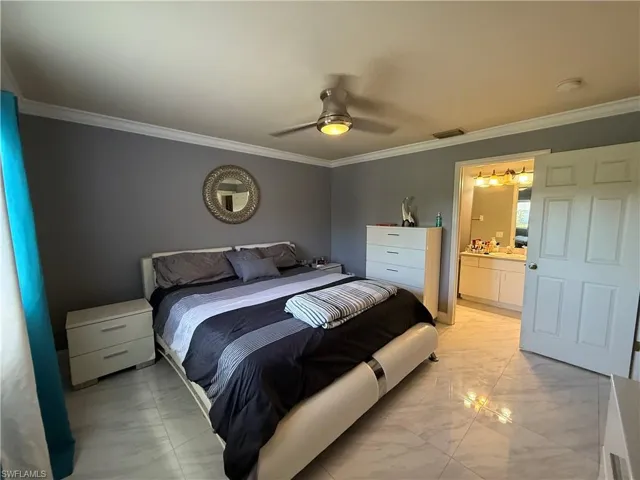 Bedroom featuring ornamental molding, light marble finish flooring, a ceiling fan, and connected bathroom