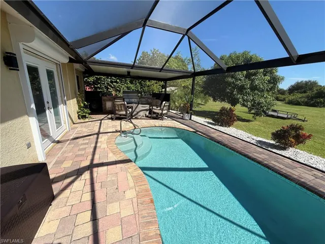 Outdoor pool featuring french doors, a lawn, glass enclosure, a patio, and a sunroom