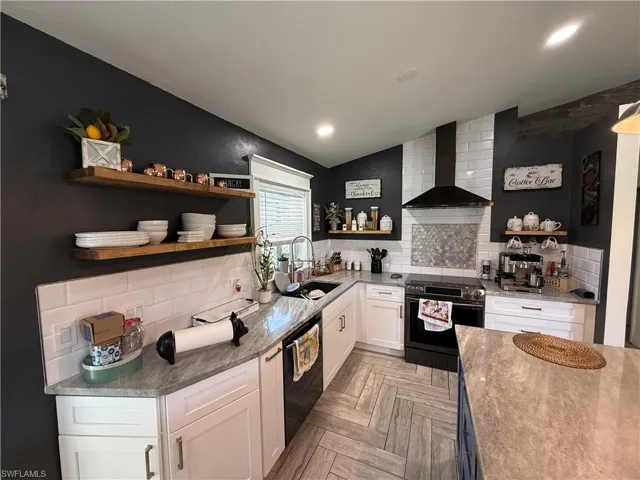 Kitchen with white cabinetry, backsplash, wall chimney exhaust hood, electric range oven, and light stone counters