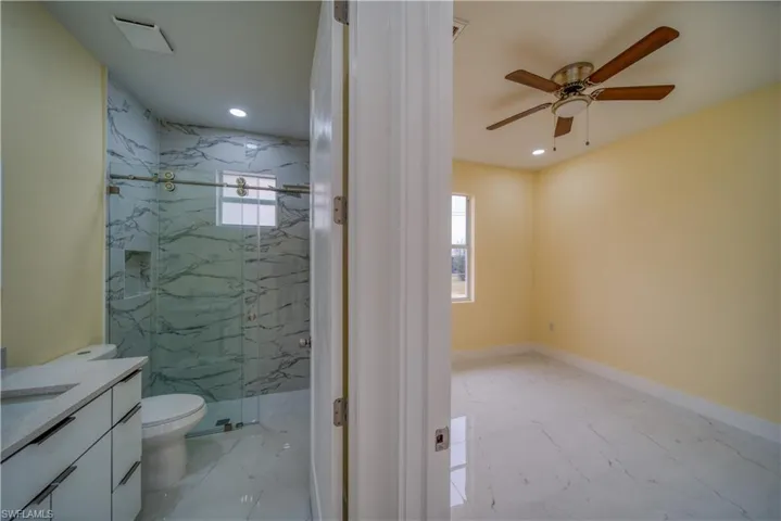 Bathroom with ceiling fan, toilet, a shower with door, and vanity