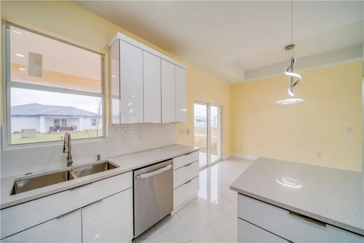 Kitchen with pendant lighting, white cabinetry, tasteful backsplash, sink, and stainless steel dishwasher