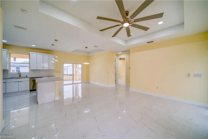 Unfurnished living room with ceiling fan, sink, and a raised ceiling