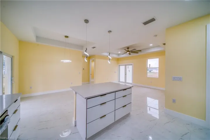 Kitchen featuring dishwasher, hanging light fixtures, a raised ceiling, white cabinetry, and a center island