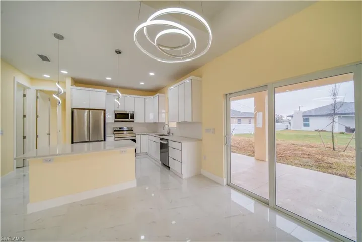 Kitchen with decorative light fixtures, sink, white cabinets, a center island, and stainless steel appliances
