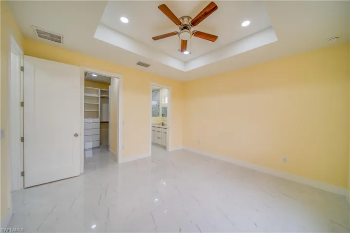 Unfurnished bedroom with a closet, a walk in closet, ensuite bath, and a raised ceiling