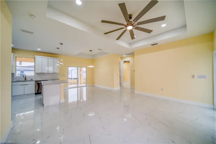 Unfurnished living room with ceiling fan, sink, a raised ceiling, and a healthy amount of sunlight