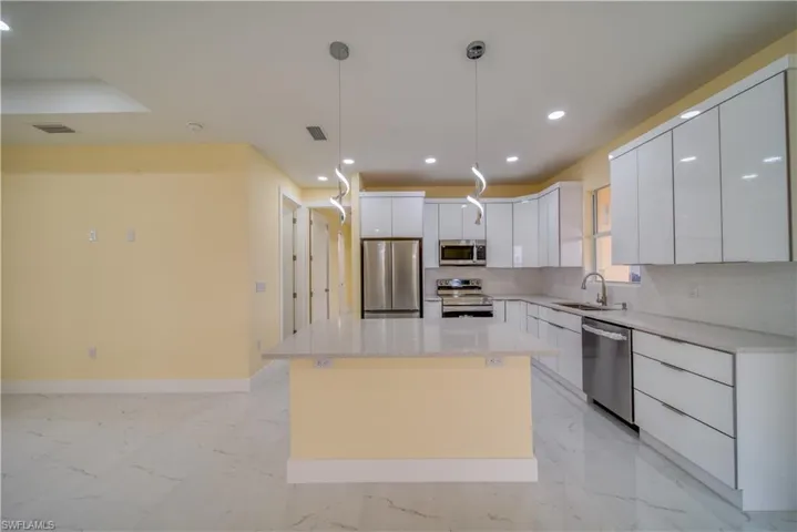 Kitchen featuring appliances with stainless steel finishes, hanging light fixtures, white cabinets, a kitchen island, and sink