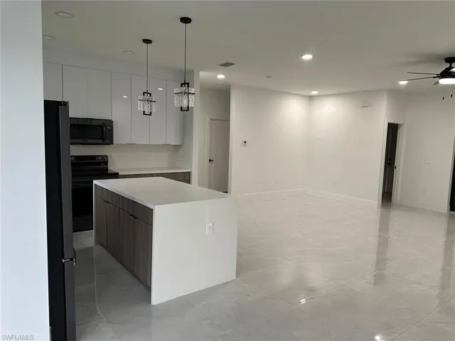 Kitchen featuring ceiling fan, decorative light fixtures, black appliances, light tile floors, and a center island