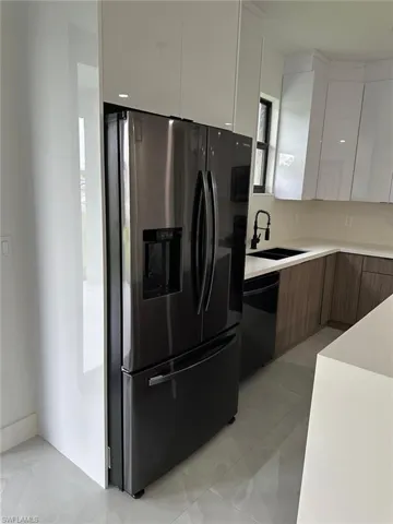 Kitchen with dishwasher, white cabinetry, stainless steel fridge, sink, and light tile floors