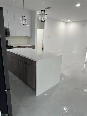 Kitchen with light tile floors, white cabinetry, a notable chandelier, and pendant lighting