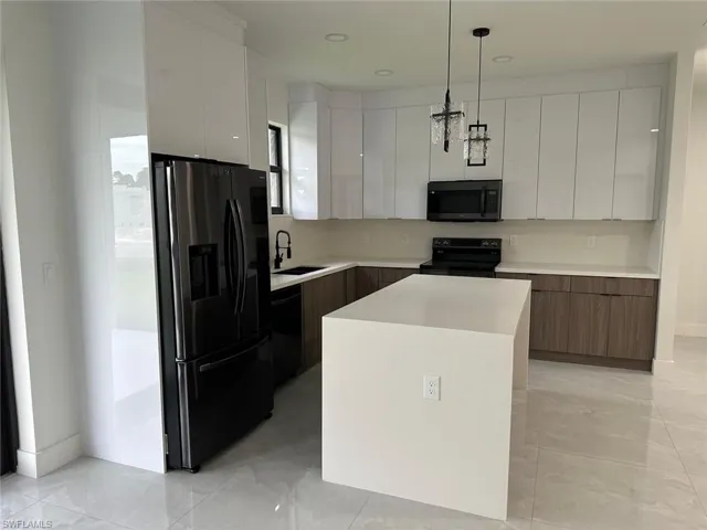 Kitchen featuring decorative light fixtures, black appliances, a kitchen island, sink, and white cabinets