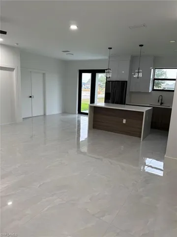 Kitchen with a wealth of natural light, black refrigerator with ice dispenser, light tile floors, and hanging light fixtures