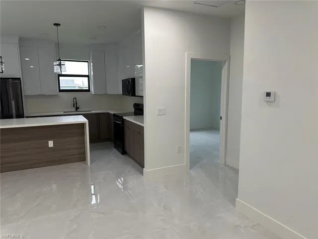 Kitchen featuring black appliances, sink, light tile floors, and pendant lighting