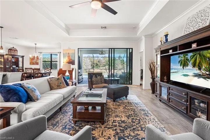 Living area featuring a raised ceiling, visible vents, crown molding, and ceiling fan