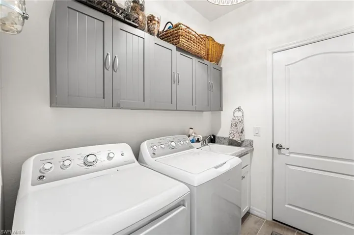 Clothes washing area featuring a sink, washing machine and dryer, and cabinet space