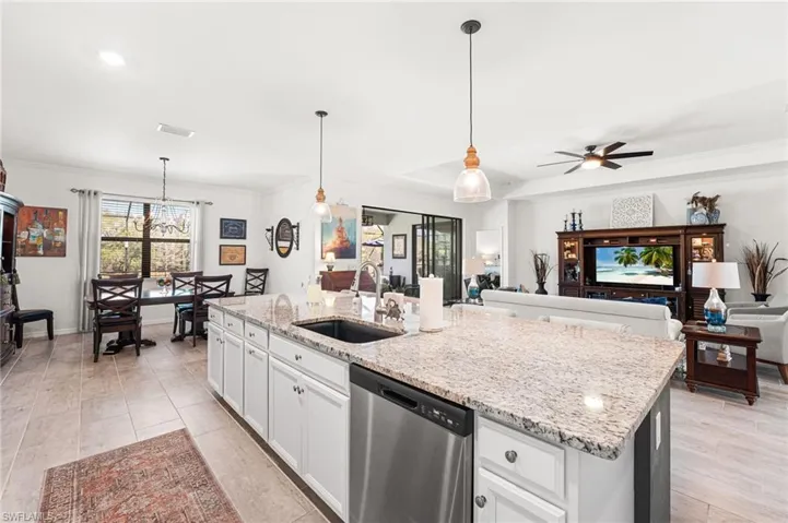 Kitchen featuring light stone counters, a sink, open floor plan, dishwasher, and an island with sink