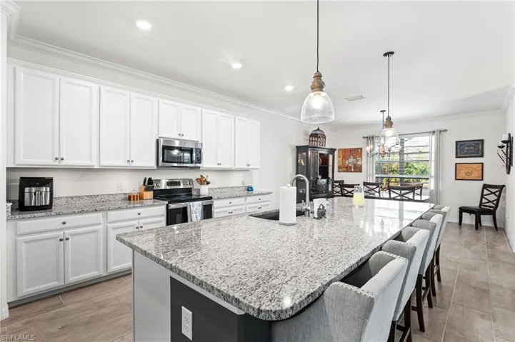 Kitchen featuring an island with sink, ornamental molding, stainless steel appliances, white cabinetry, and a sink