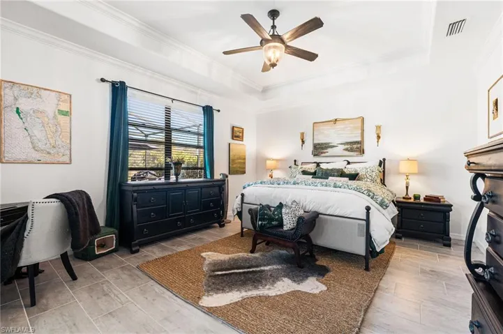 Bedroom featuring ceiling fan, a raised ceiling, visible vents, and ornamental molding