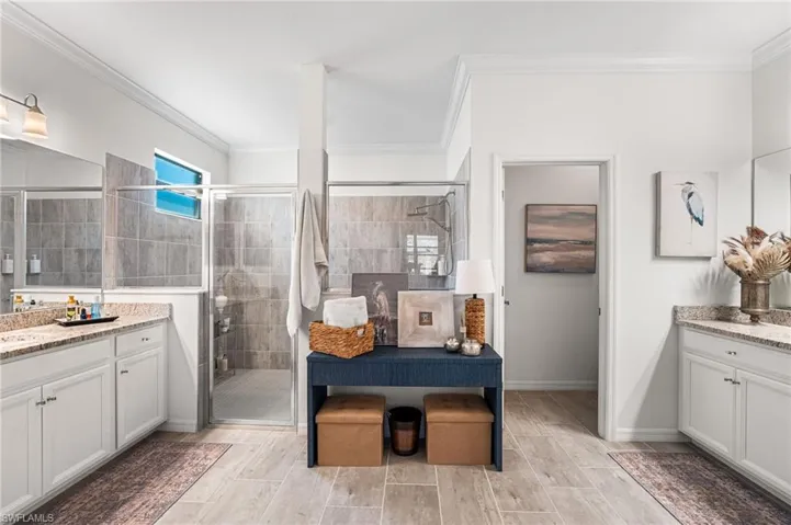 Bathroom with a stall shower, baseboards, crown molding, wood finish floors, and two vanities