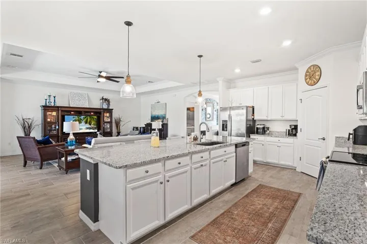 Kitchen featuring a tray ceiling, appliances with stainless steel finishes, light wood-style floors, a kitchen island with sink, and a sink