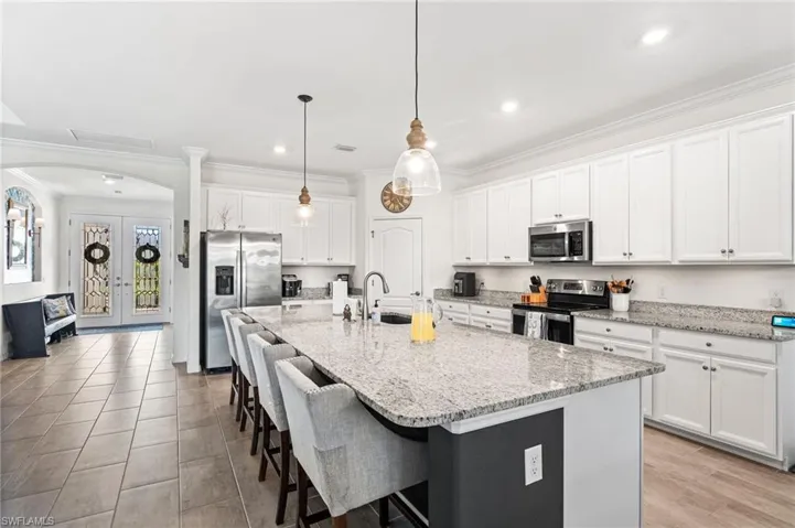 Kitchen featuring arched walkways, a sink, appliances with stainless steel finishes, ornamental molding, and a kitchen bar