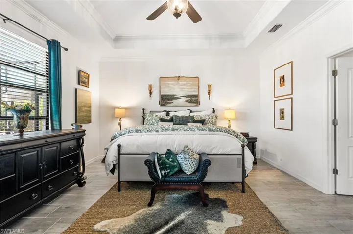 Bedroom featuring a tray ceiling, visible vents, baseboards, and crown molding