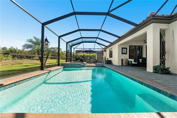 View of pool featuring glass enclosure, a pool with connected hot tub, and a patio