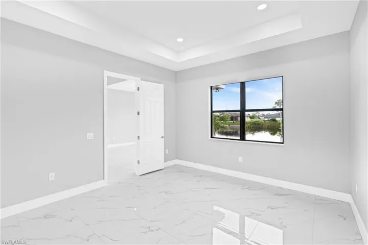 Unfurnished bedroom featuring light marble finish flooring, a raised ceiling, and recessed lighting