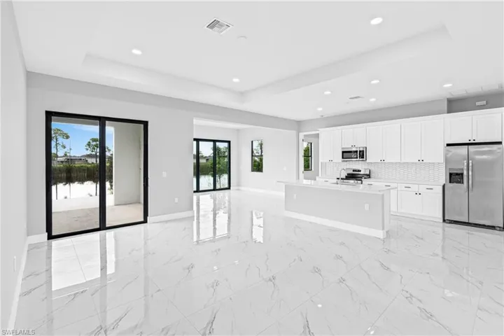 Kitchen with light marble finish flooring, appliances with stainless steel finishes, a raised ceiling, open floor plan, and recessed lighting