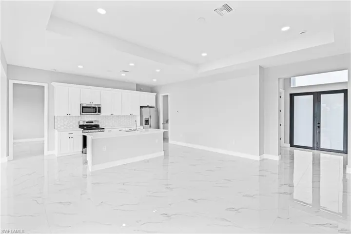 Kitchen featuring a raised ceiling, light marble finish flooring, a center island with sink, and recessed lighting