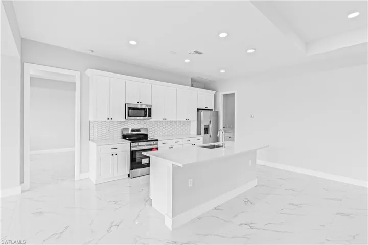 Kitchen with white cabinets, appliances with stainless steel finishes, a kitchen island with sink, light marble finish floors, and recessed lighting