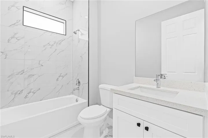Bathroom with washtub / shower combination, vanity, and marble finish flooring