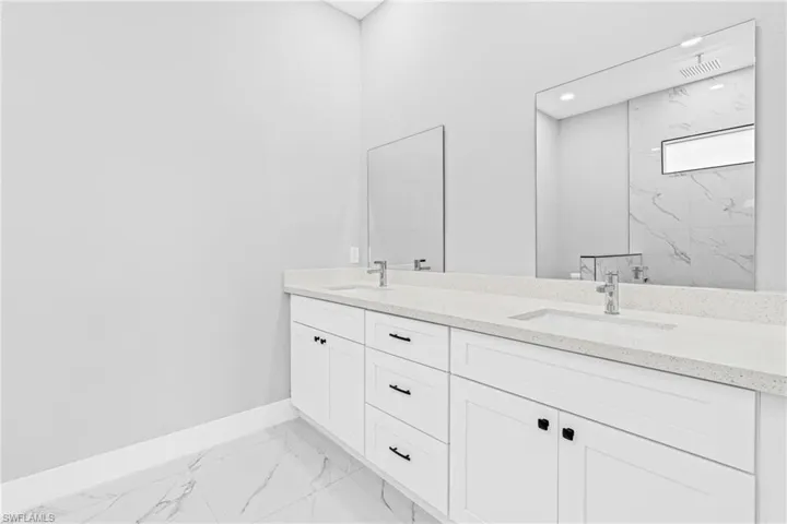 Bathroom featuring light marble finish flooring, double vanity, and a marble finish shower