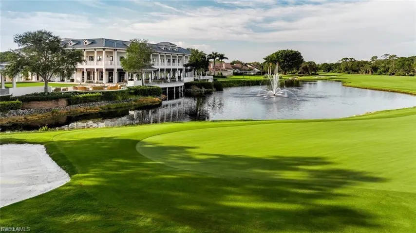 Expansive golf course green with sand trap, bordering a tranquil pond featuring a central fountain