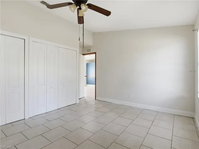 Unfurnished bedroom featuring two closets, a ceiling fan, vaulted ceiling, and light tile patterned floors