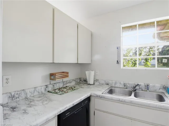Kitchen with black dishwasher, light countertops, and white cabinetry