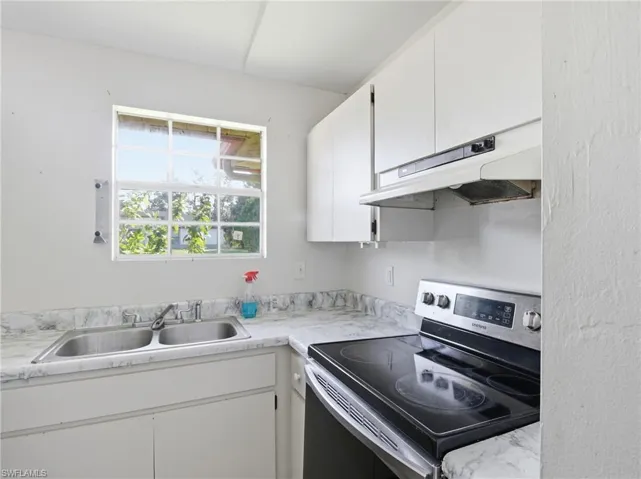 Kitchen with stainless steel electric stove, white cabinetry, and under cabinet range hood