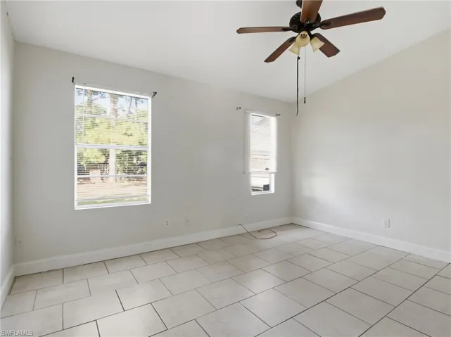 Empty room featuring healthy amount of natural light, a ceiling fan, light tile patterned floors, and vaulted ceiling