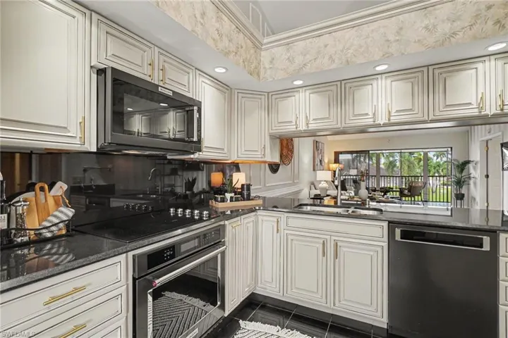White cabinetry with gold-tone hardware, dark countertop surfaces, built-in microwave, integrated cooktop and oven, and undermount sink