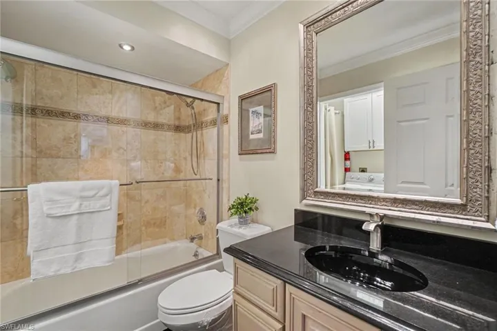 Bathtub with tiled surround, glass shower enclosure, and single vanity with a dark countertop and undermount sink