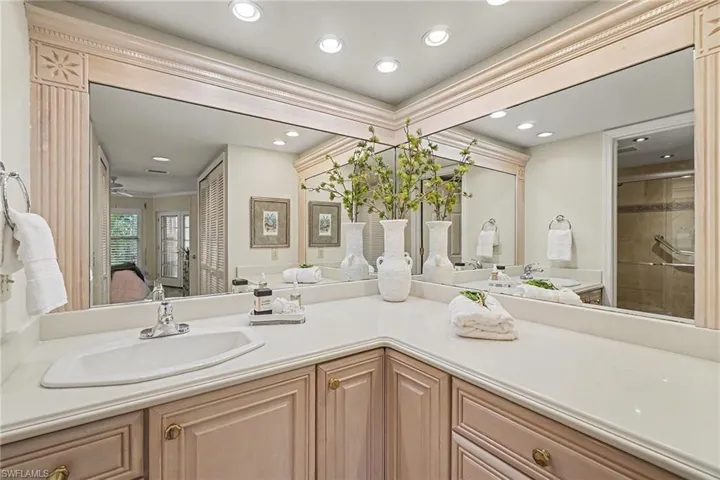 Double vanity with undermount sinks, expansive countertop, framed mirrors, recessed lighting, and wood-finish cabinetry