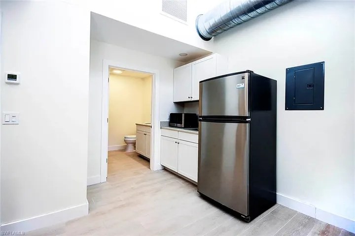Kitchen area with freestanding refrigerator, white cabinetry, electric panel, and light wood finished floors