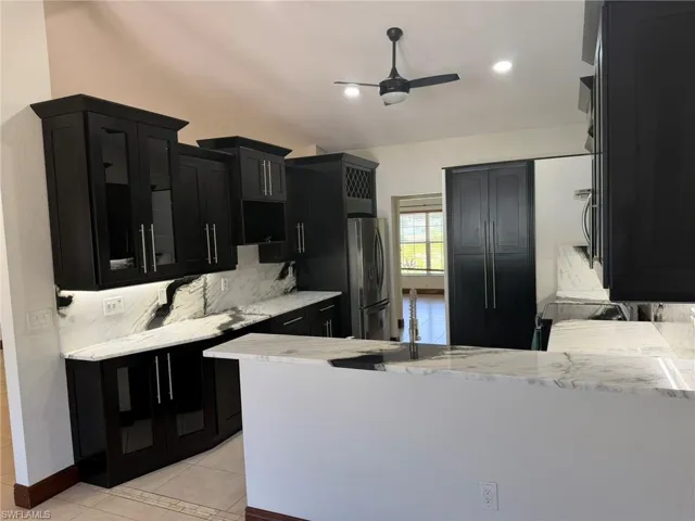 Contemporary kitchen featuring dark wood cabinetry, white stone countertops, integrated stainless steel appliances, a bar-height counter, and recessed lighting