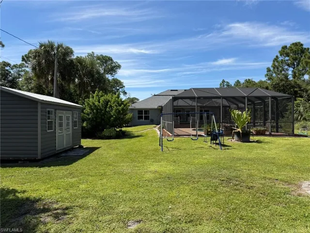 Expansive green space with an enclosed patio, a dedicated storage shed, and mature foliage