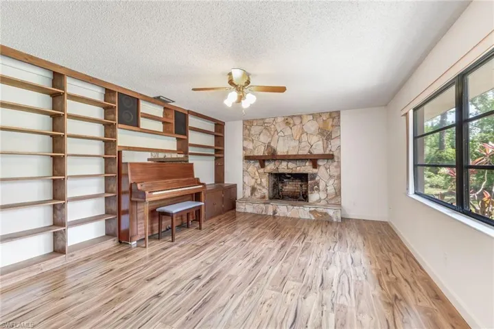 Unfurnished living room with ceiling fan, a stone fireplace and built in shelving