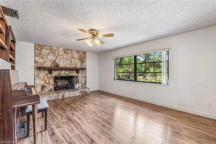 Living room with vinyl wood-like floors, a stone fireplace and ceiling fan