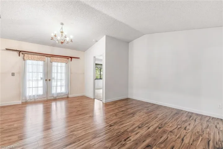Formal dining area or living area featuring an inviting chandelier, vinyl wood-like flooring, and lofted ceiling. French doors take you to the patio. Single bedroom door shown here takes you into the master bedroom.