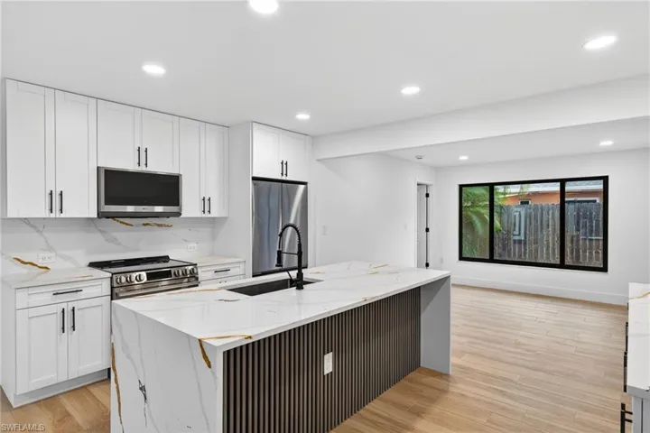 Kitchen with light stone counters, light wood-type flooring, white cabinets, recessed lighting, and appliances with stainless steel finishes